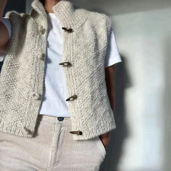 Gilet in lana beige con bottoni in legno, indossato su maglietta bianca e pantaloni a righe. Moda autunnale, abbigliamento casual elegante.