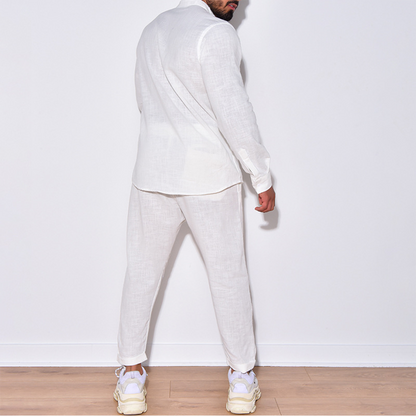 Uomo in abito di lino bianco, camicia e pantaloni, scarpe da ginnastica bianche, posa di spalle su sfondo bianco. Moda maschile estiva elegante.