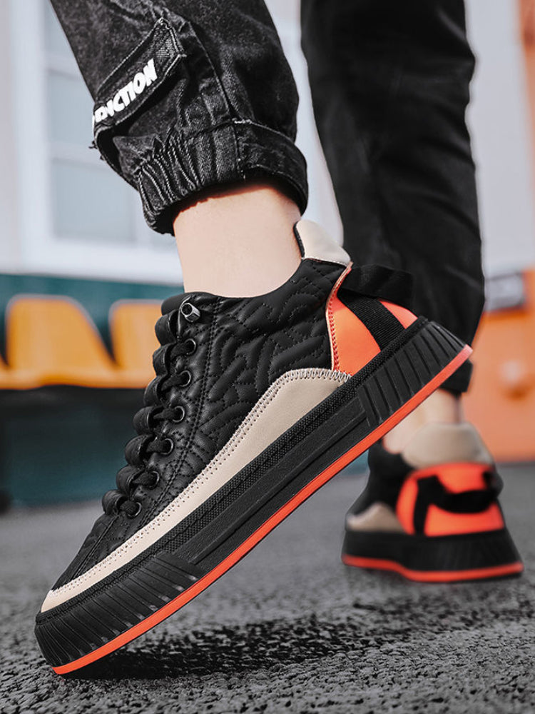 Scarpe da ginnastica nere e arancioni su pavimento asfaltato, design moderno con suola spessa, indossate da persona in jeans neri.