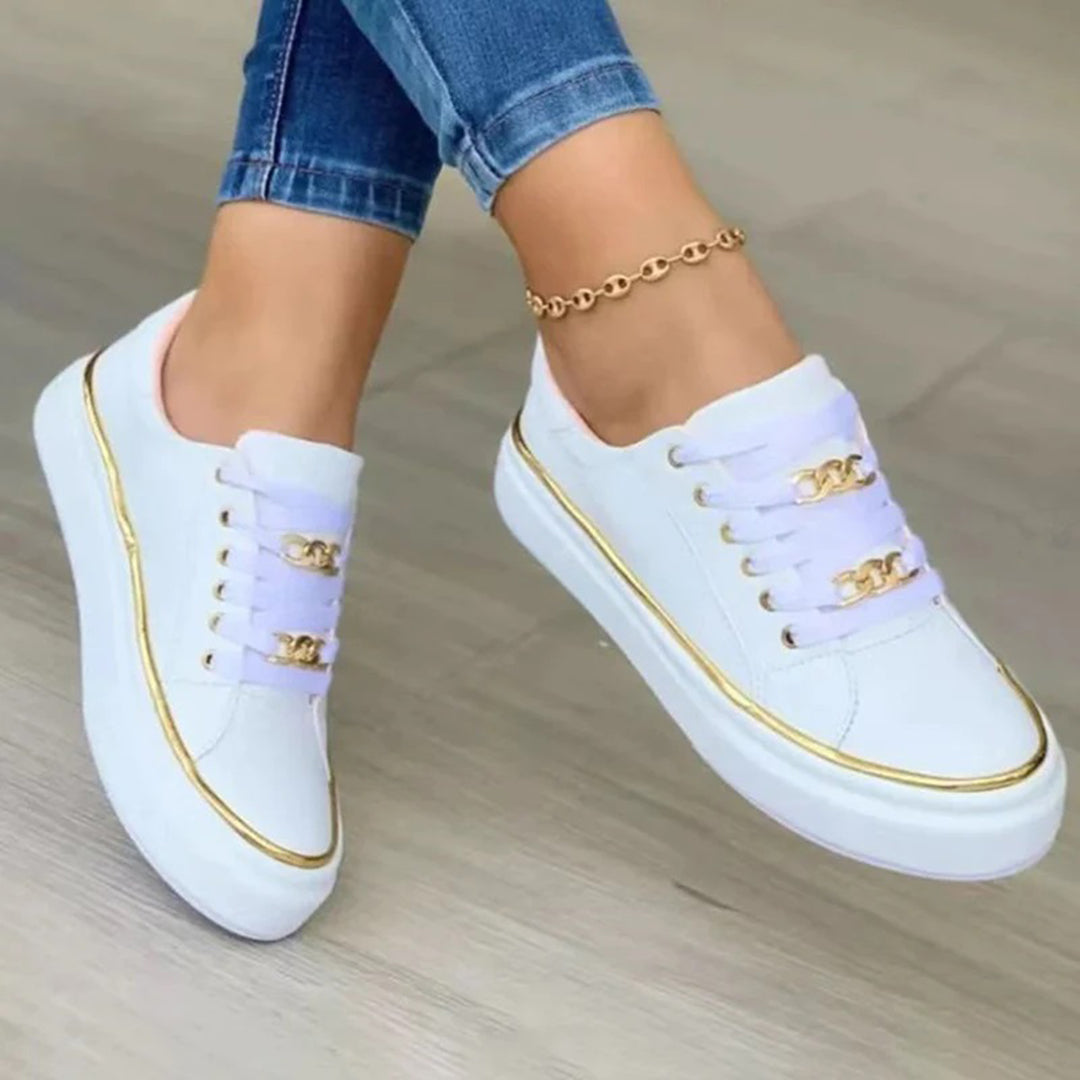 Scarpe da ginnastica bianche con dettagli dorati, indossate con jeans. Sneakers moda donna, stile casual, tendenza calzature 2023.