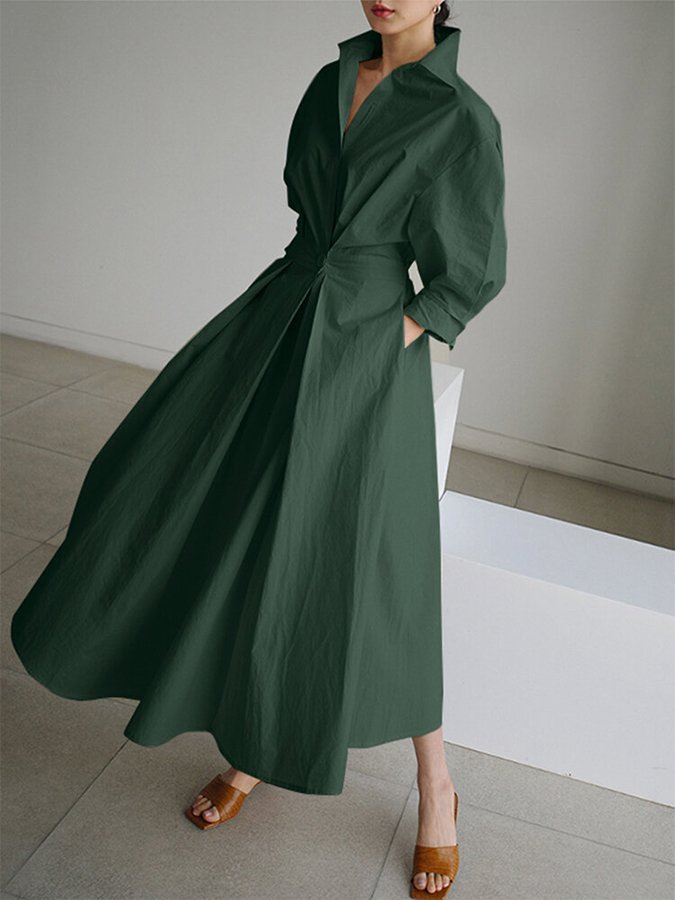 Abito lungo verde scuro elegante con colletto alto e maniche lunghe, indossato con sandali marroni su pavimento chiaro. Moda femminile sofisticata.