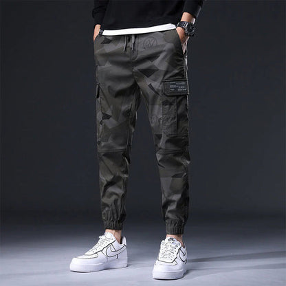 Pantaloni cargo mimetici da uomo, stile casual, con tasche laterali, indossati con sneakers bianche Nike. Moda streetwear moderna.