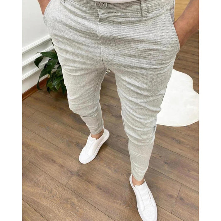 Pantaloni grigi eleganti da uomo, abbinati a scarpe bianche casual, su pavimento in legno. Stile moderno e raffinato per look quotidiano.