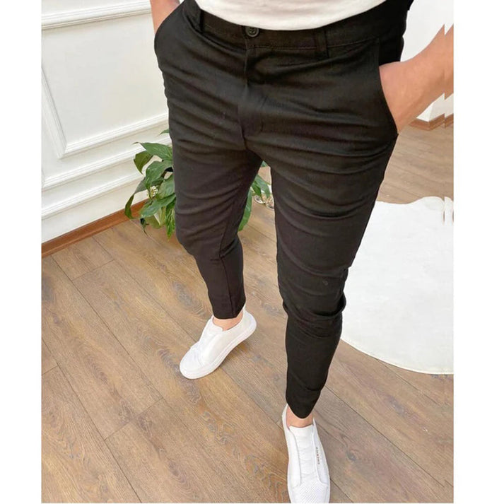 Uomo in pantaloni neri slim fit e scarpe bianche su pavimento in legno. Moda maschile casual, abbigliamento elegante, stile moderno.