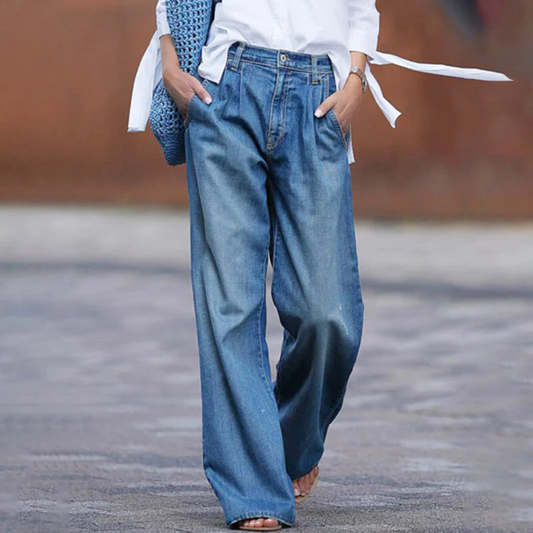 Jeans larghi da donna in denim blu, stile casual, abbinati a camicia bianca e borsa a rete blu. Moda streetwear femminile.