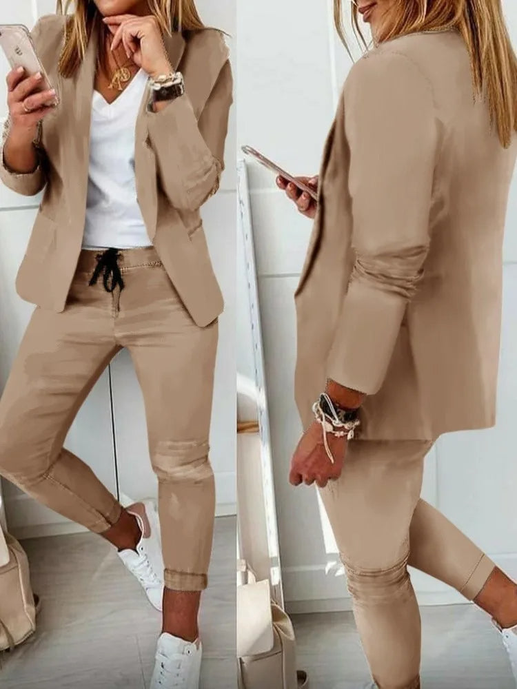 Donna in abito beige casual, giacca e pantaloni, con smartphone. Look moderno e chic, perfetto per ufficio o incontri informali. Scarpe bianche.