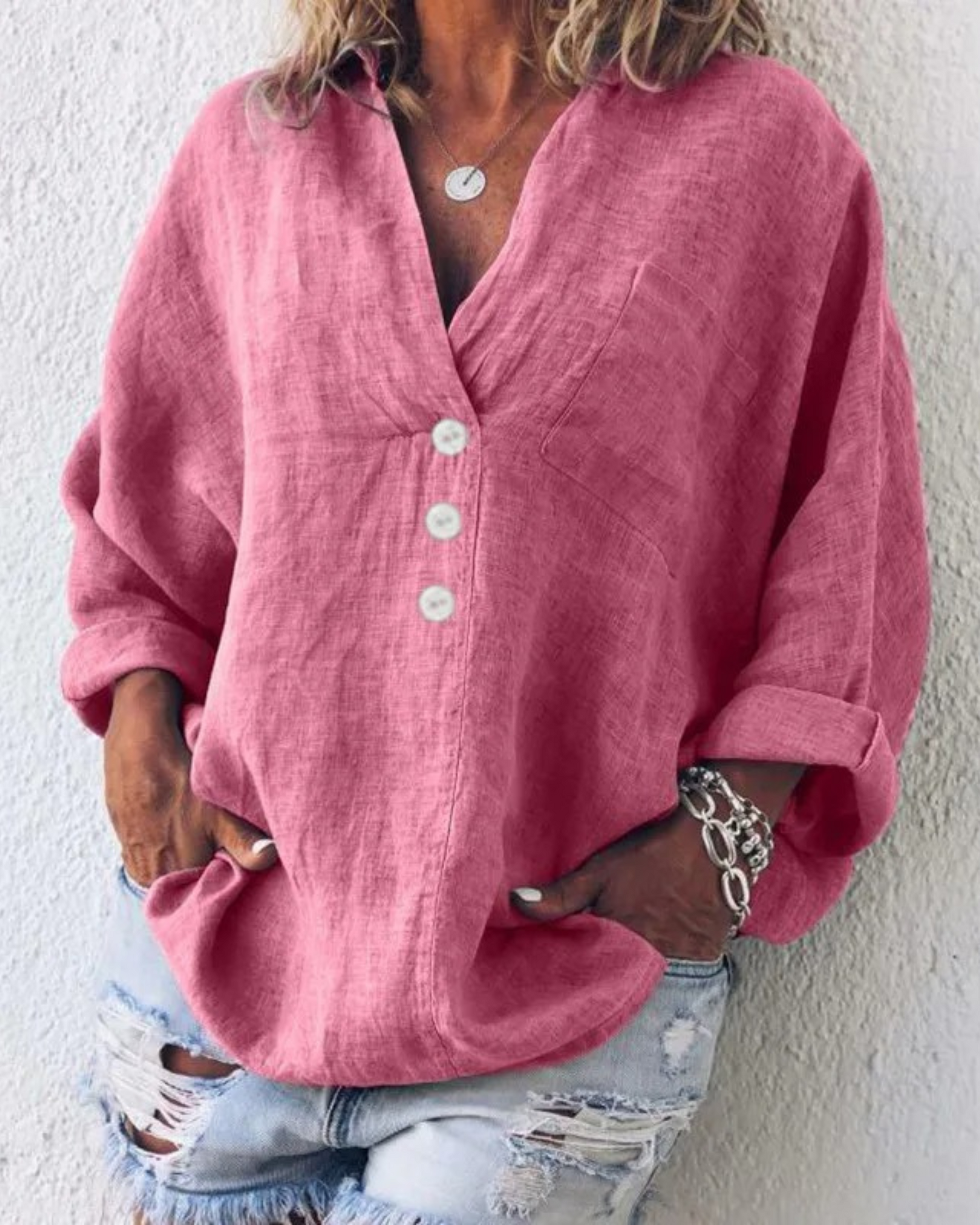 Camicia di lino rosa donna con bottoni bianchi, maniche lunghe arrotolate, abbinata a jeans strappati. Stile casual, moda estiva.