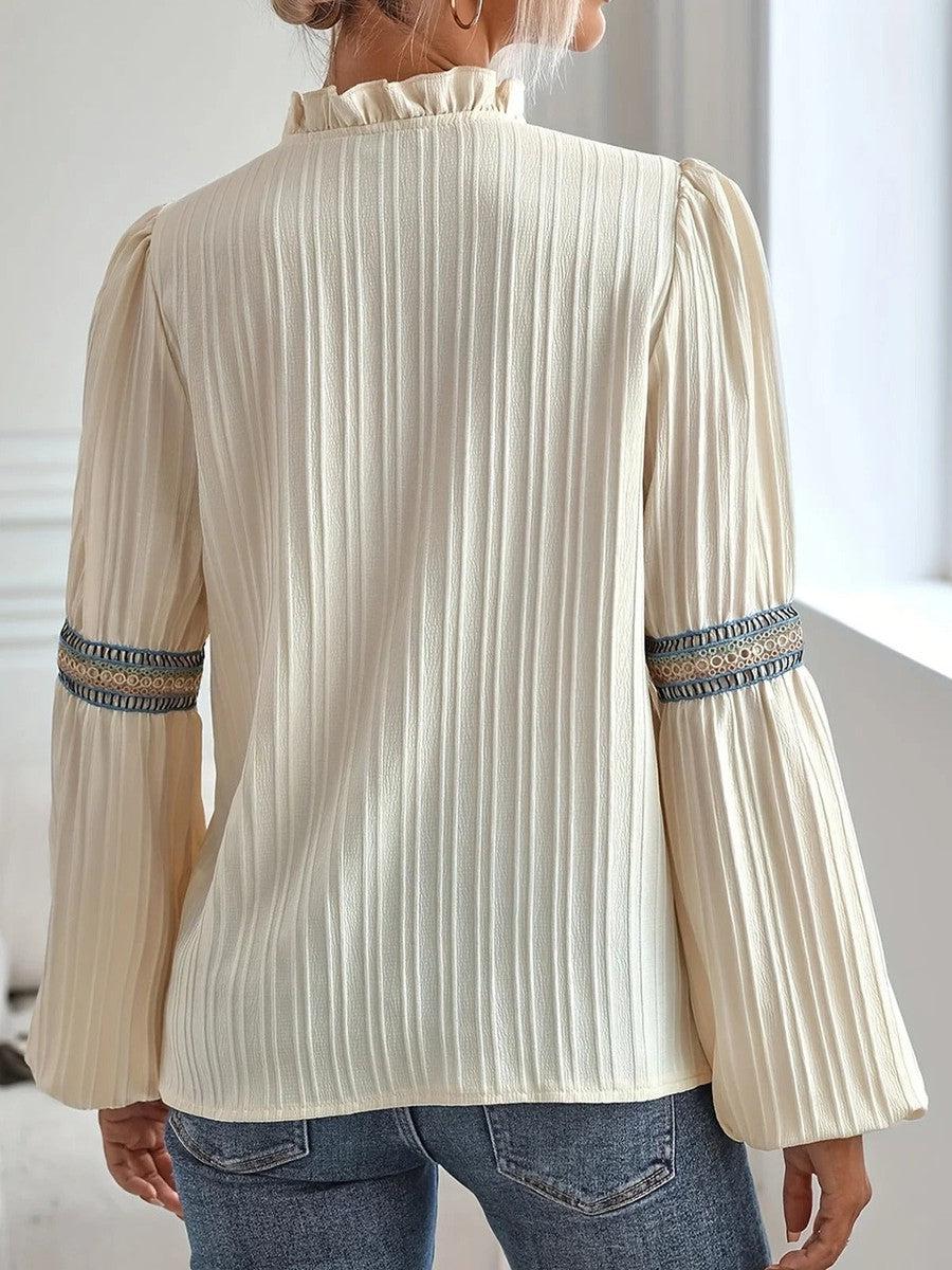 Blusa bianca a maniche lunghe con dettagli ricamati, tessuto plissettato, collo alto, indossata con jeans. Moda donna elegante e casual.