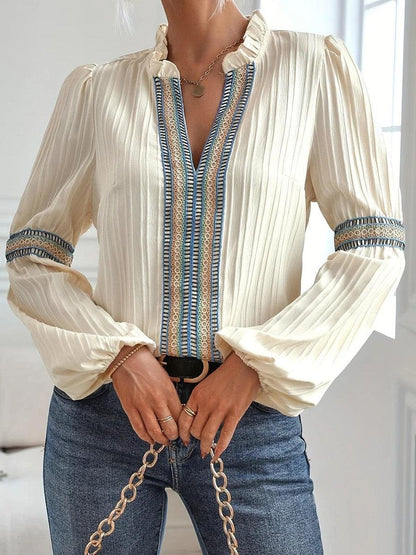Camicia elegante donna in seta avorio con dettagli ricamati blu, maniche lunghe a sbuffo, abbinata a jeans. Moda femminile chic e sofisticata.