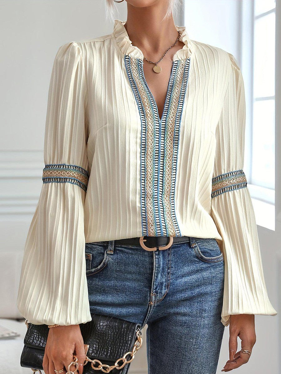 Blusa elegante crema con dettagli ricamati blu, maniche lunghe a sbuffo, abbinata a jeans e borsa nera. Moda femminile casual chic.