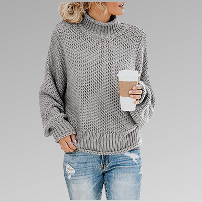 Donna con maglione grigio a collo alto, tiene una tazza di caffè. Indossa jeans strappati. Moda casual autunnale, stile urbano.
