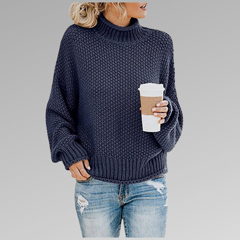 Maglione blu a maglia grossa, collo alto, indossato con jeans strappati. Donna con caffè da asporto. Moda casual autunnale.