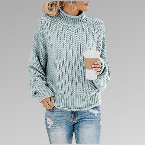Donna con maglione a maglia verde menta, jeans strappati, tiene una tazza di caffè. Moda casual autunnale, abbigliamento femminile trendy.