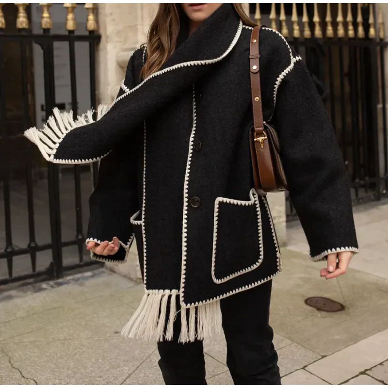 Donna con cappotto nero oversize con frange bianche, dettagli cuciti, borsa marrone a tracolla. Moda autunnale, street style elegante.