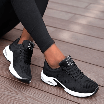 Scarpe da ginnastica nere da donna su pavimento in legno, design moderno e traspirante, ideali per sport e tempo libero.