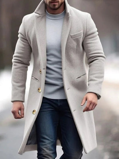 Uomo con cappotto invernale beige elegante, maglione grigio e jeans, cammina all'aperto. Moda maschile, abbigliamento invernale, stile urbano.