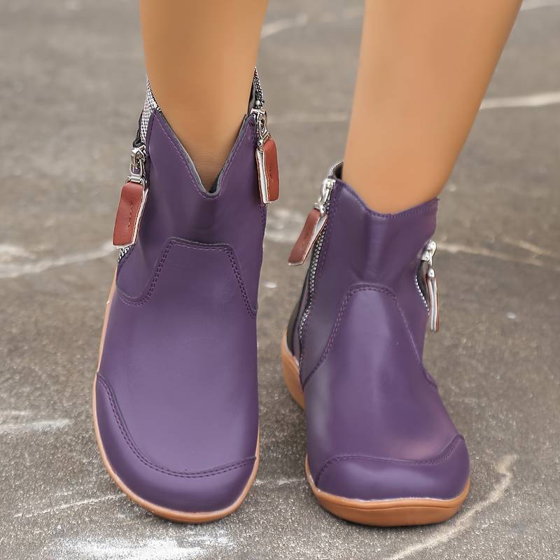 Stivaletti viola con cerniere laterali e suola marrone, indossati su pavimento grigio. Scarpe moda donna, calzature autunnali eleganti e comode.