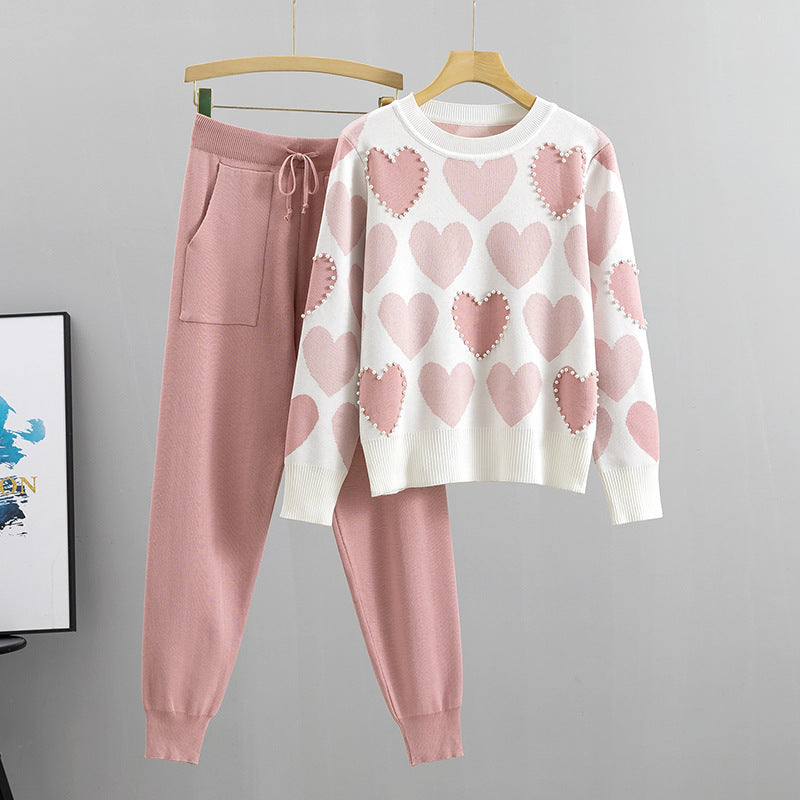 Set coordinato donna: maglione bianco con cuori rosa e pantaloni rosa. Moda casual, abbigliamento comodo, stile autunnale.