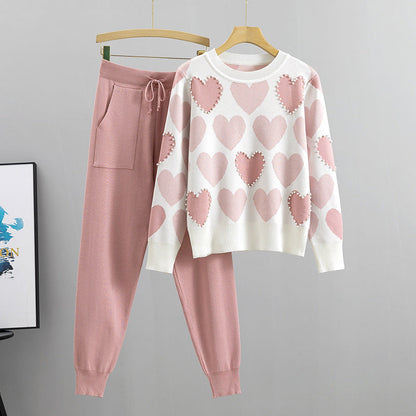 Set coordinato donna: maglione bianco con cuori rosa e pantaloni rosa. Moda casual, abbigliamento comodo, stile autunnale.
