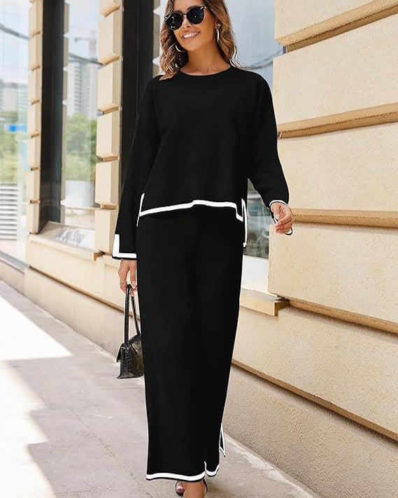 Donna con occhiali da sole indossa un elegante completo nero con dettagli bianchi, cammina su un marciapiede urbano. Moda autunnale, stile casual chic.