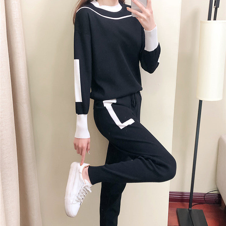 Donna in tuta nera con dettagli bianchi, posa davanti a uno specchio. Indossa sneakers bianche. Moda casual, abbigliamento comodo, stile moderno.