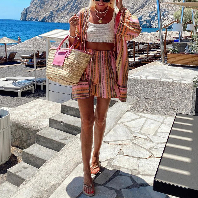 Donna in spiaggia con abbigliamento estivo colorato, borsa di paglia e sandali. Mare e lettini sullo sfondo. Look estivo alla moda.