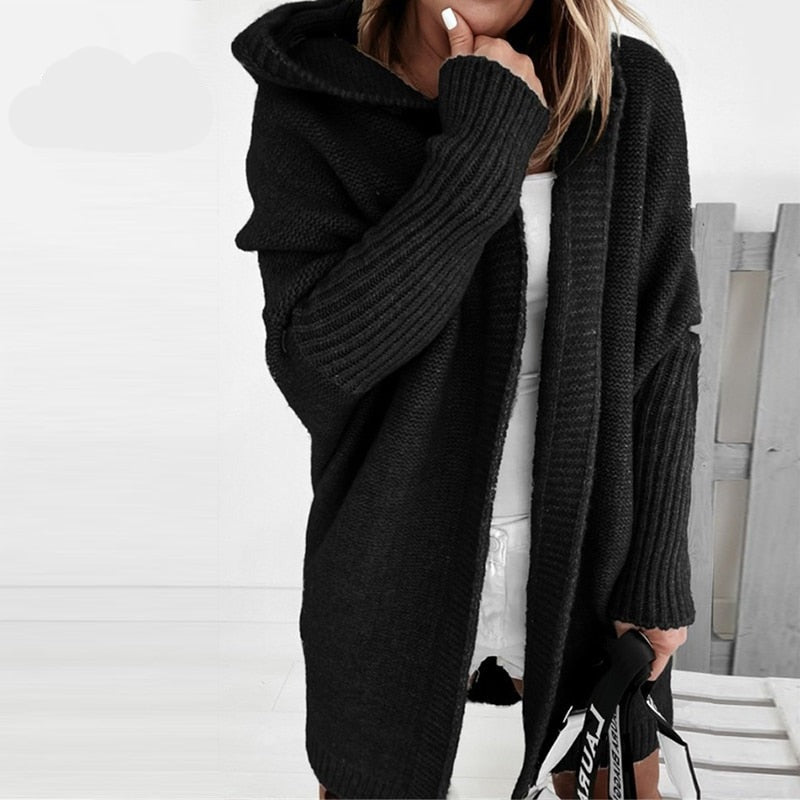 Donna con cardigan nero oversize a maglia, cappuccio e maniche lunghe, abbinato a vestito bianco. Stile casual autunnale.