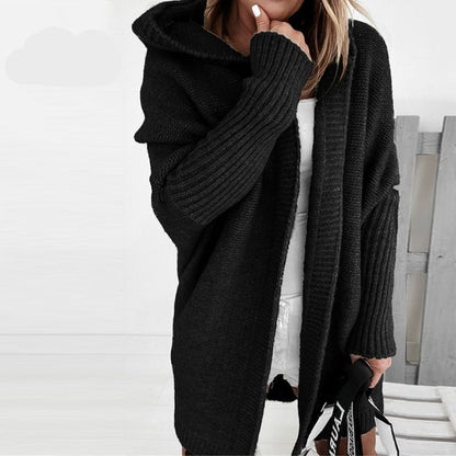 Donna con cardigan nero oversize a maglia, cappuccio e maniche lunghe, abbinato a vestito bianco. Stile casual autunnale.