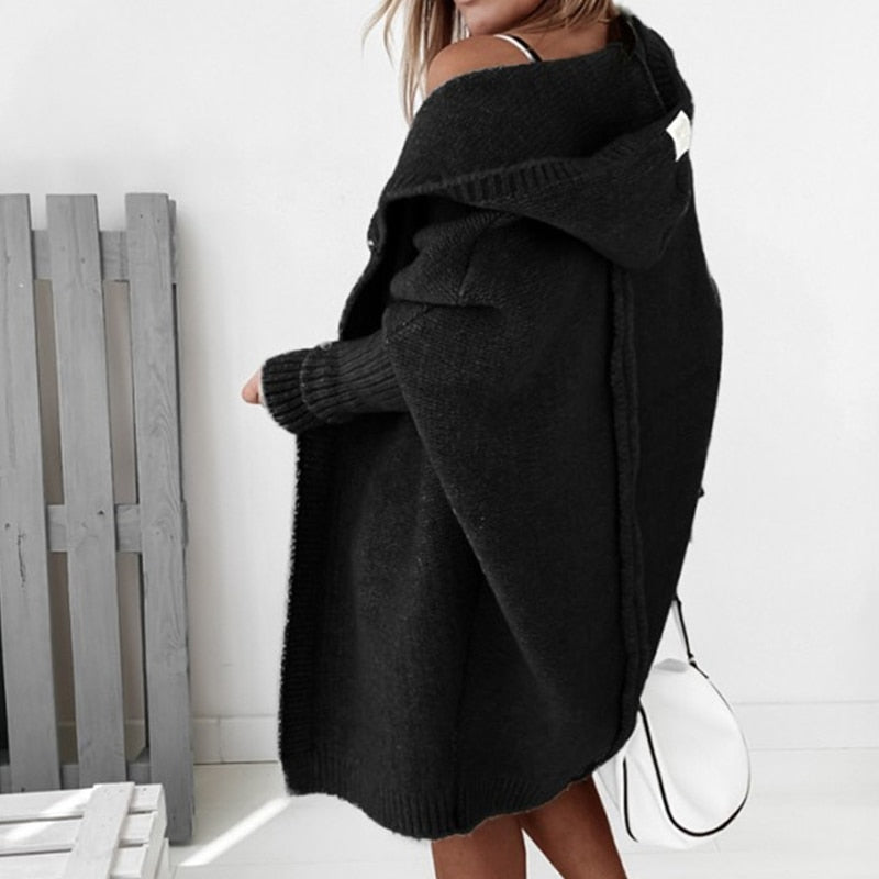 Donna con cappotto nero oversize, cappuccio, maniche lunghe, in ambiente minimalista. Moda autunnale, stile casual chic, tendenze abbigliamento.