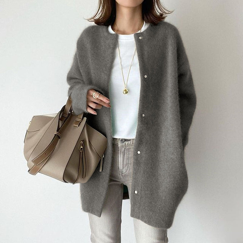 Donna con cardigan grigio oversize, maglietta bianca, jeans chiari e borsa beige. Moda autunnale casual chic, outfit elegante e moderno.