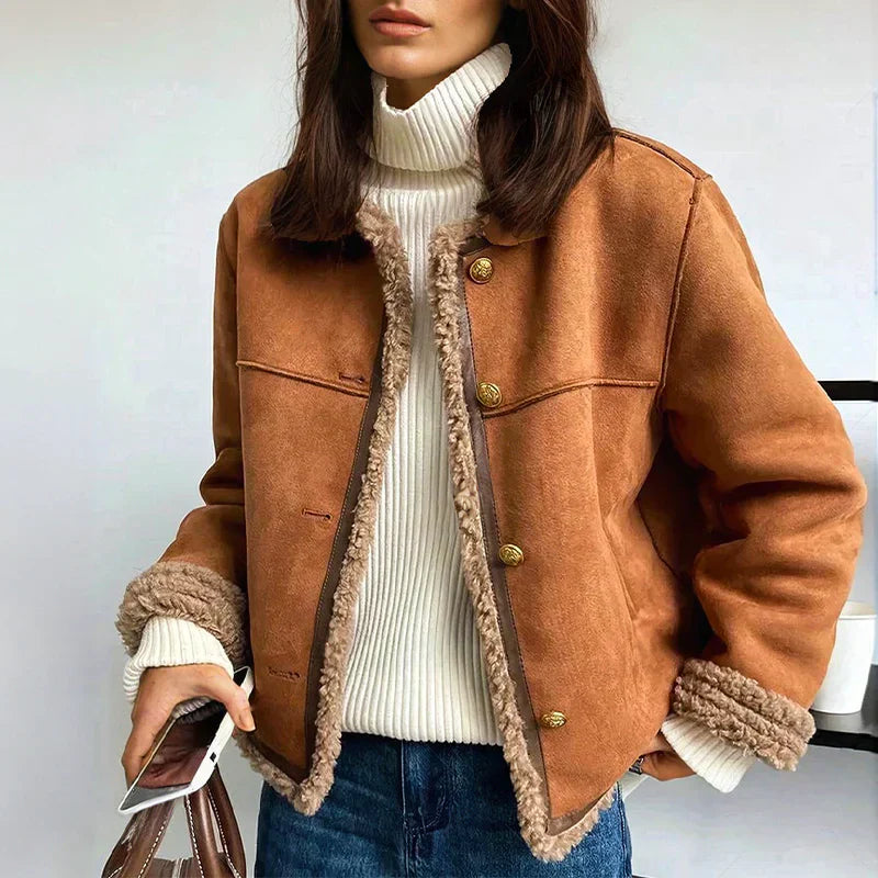 Donna con giacca invernale marrone con bottoni dorati, maglione a collo alto bianco, jeans blu, smartphone in mano. Moda autunno inverno.