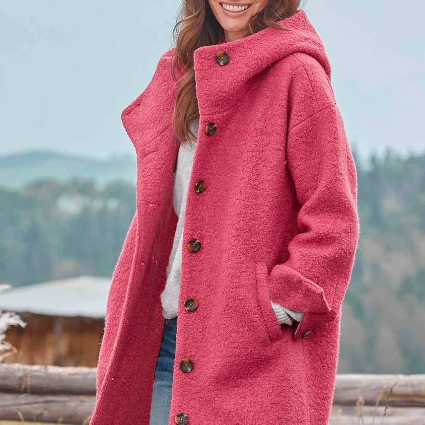 Donna sorridente con cappotto rosa in lana, bottoni marroni, sfondo montano. Moda invernale, abbigliamento caldo, stile casual chic.