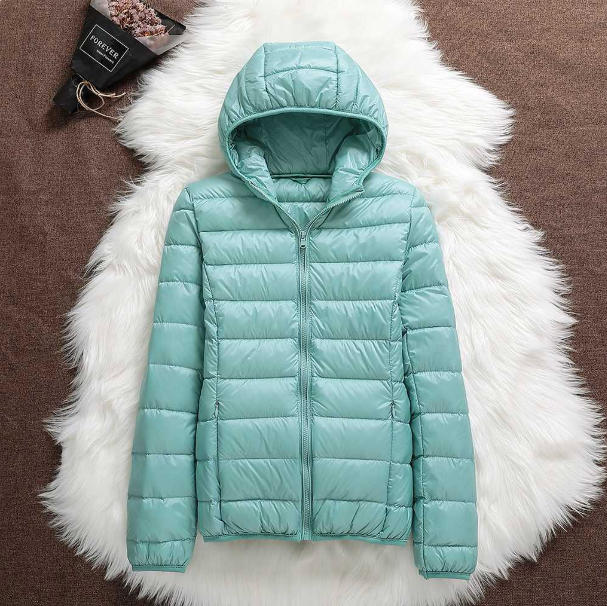 Giacca invernale imbottita verde menta su sfondo di pelliccia bianca, con cappuccio e zip frontale. Moda donna, abbigliamento caldo e trendy.