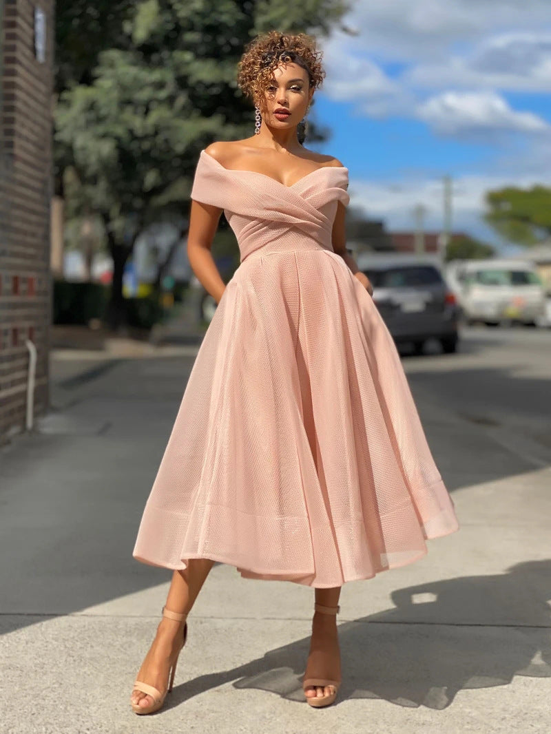 Donna in abito rosa elegante su strada cittadina, con cielo blu e nuvole sullo sfondo. Moda femminile, abbigliamento chic, stile urbano.