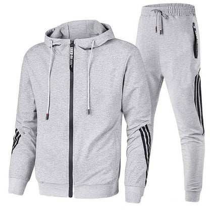 Tuta sportiva grigia con cappuccio, zip frontale e pantaloni con bande nere laterali. Abbigliamento casual uomo, comodo e moderno.