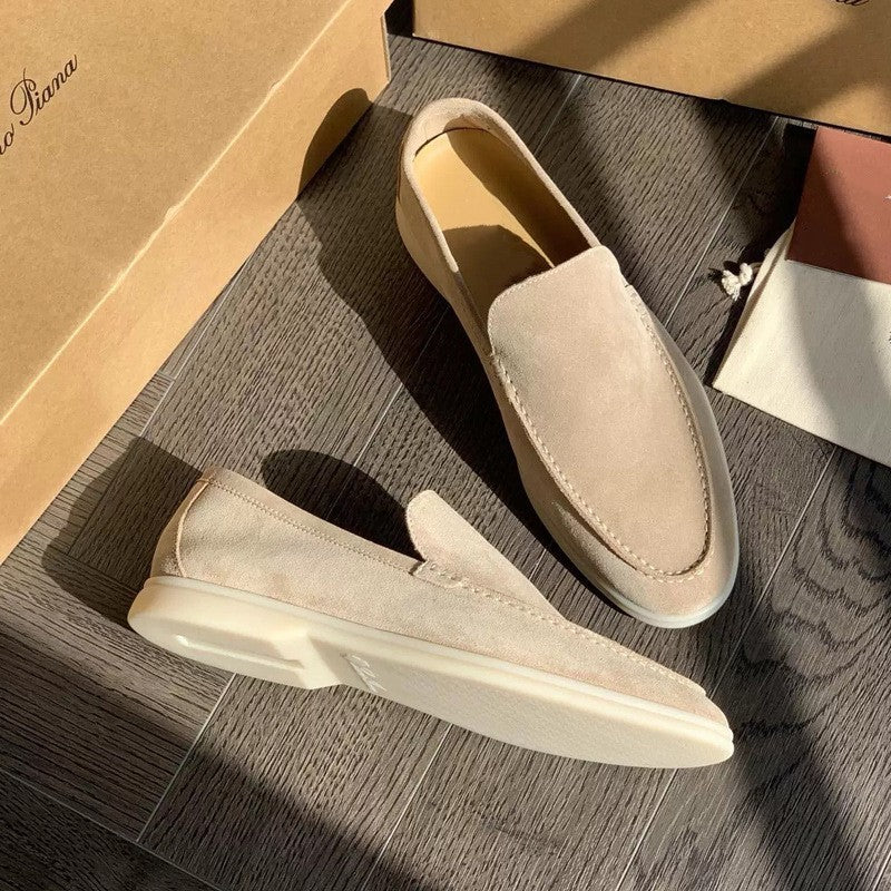 Mocassini beige in pelle scamosciata su pavimento in legno, illuminati dalla luce solare. Scarpe eleganti da uomo, stile casual, moda italiana.