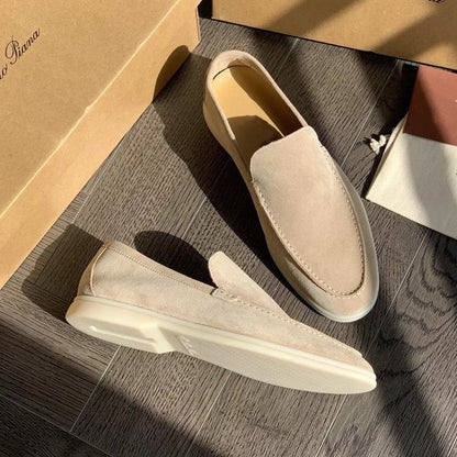 Mocassini beige in pelle scamosciata su pavimento in legno, illuminati dalla luce solare. Scarpe eleganti da uomo, stile casual, moda italiana.
