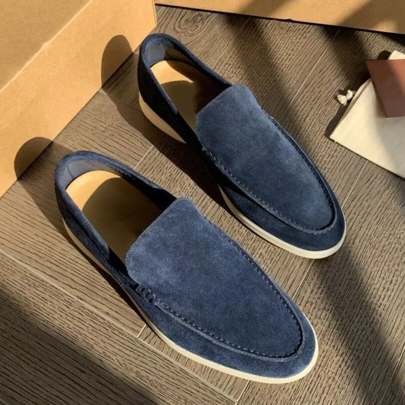 Scarpe mocassini uomo in pelle scamosciata blu, suola bianca, su pavimento in legno. Eleganti e casual, ideali per moda maschile e comfort.