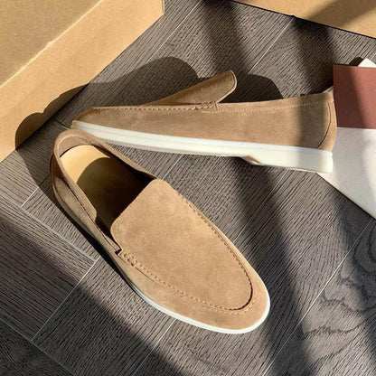 Mocassini beige da uomo in pelle scamosciata su pavimento in legno, con suola bianca. Scarpe eleganti e casual, ideali per moda maschile.