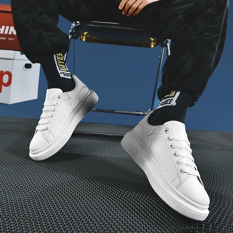 Scarpe da ginnastica bianche su sfondo blu, indossate con calzini neri e pantaloni sportivi. Moda casual, tendenze scarpe 2023.