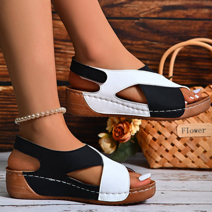 Sandali donna bicolore nero e bianco con zeppa in legno, cinturino alla caviglia, su sfondo rustico con cesto di fiori. Scarpe estive eleganti.