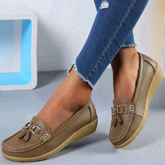 Scarpe mocassini donna in pelle marrone con nappine, suola comoda, indossate con jeans strappati. Calzature eleganti e casual per ogni occasione.