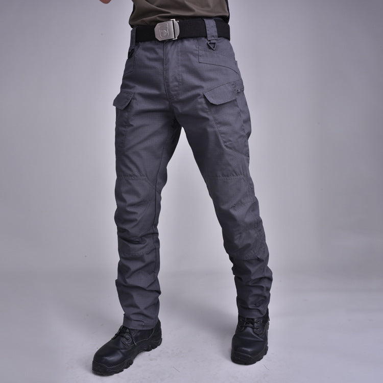 Pantaloni tattici grigi con tasche cargo, cintura nera e stivali militari. Abbigliamento outdoor resistente, ideale per escursionismo e attività all'aperto.