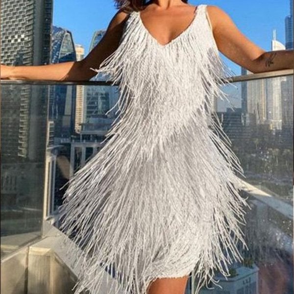 Abito bianco con frange scintillanti, indossato su terrazza con vista su skyline urbano. Moda elegante, stile glamour, tendenza abbigliamento serale.