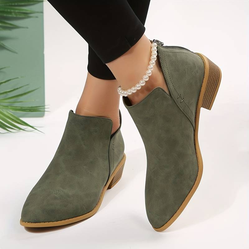 Stivaletti verdi da donna in pelle scamosciata, tacco basso, indossati con pantaloni neri e cavigliera di perle. Moda autunnale elegante.