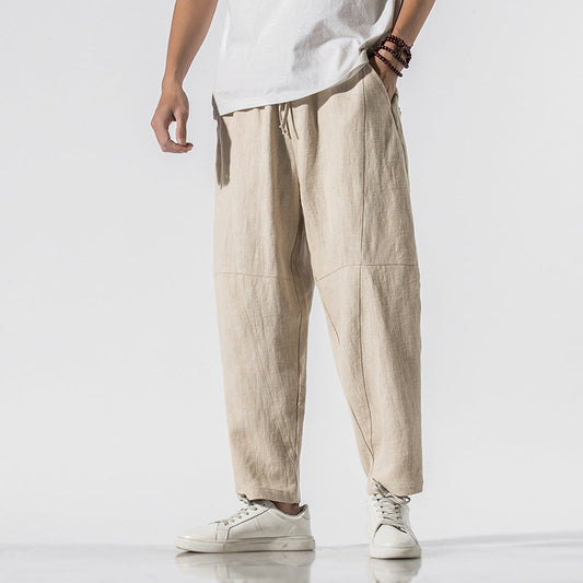Pantaloni larghi in lino beige, stile casual, indossati con sneakers bianche. Moda uomo estiva, abbigliamento comodo e traspirante.