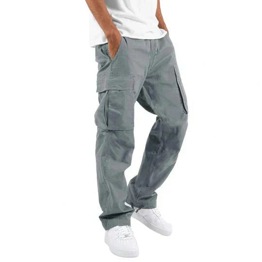 Pantaloni cargo grigi da uomo, tasche multiple, stile casual, abbinati a scarpe bianche e maglietta bianca. Moda maschile urbana.