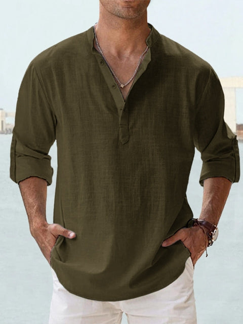 Camicia uomo verde oliva in lino, maniche lunghe arrotolate, collo alla coreana, abbinata a pantaloni bianchi. Stile casual estivo elegante.
