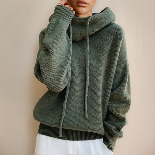 Maglione oversize verde oliva con cappuccio e lacci, indossato da una persona su sfondo neutro. Moda autunnale, abbigliamento casual elegante.