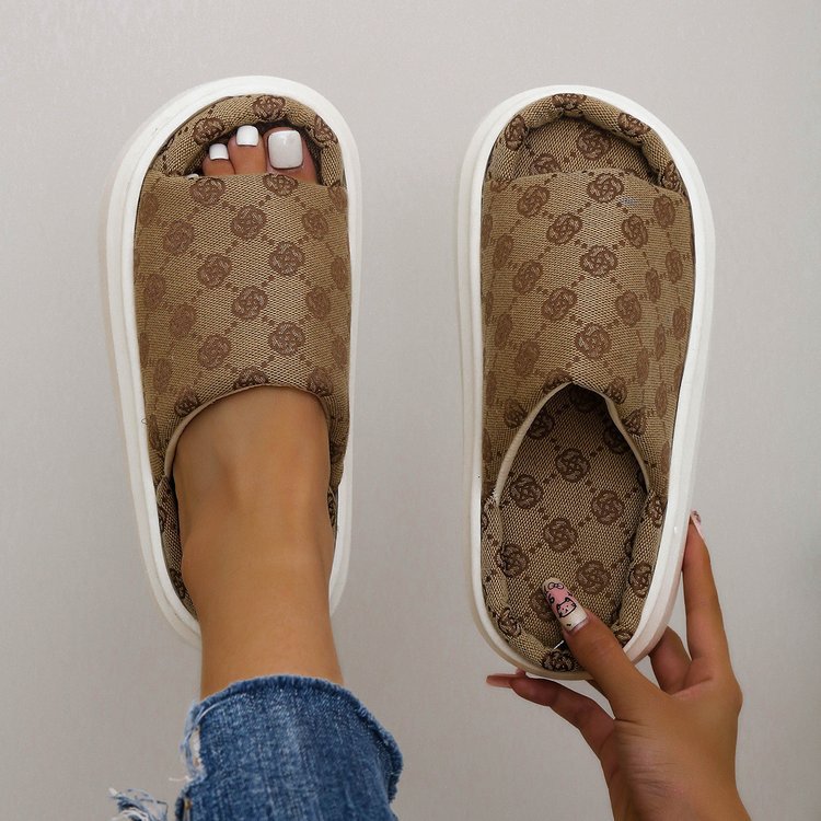 Pantofole marroni con motivo a logo, indossate su piede con unghie curate, jeans. Scarpe da casa eleganti, moda comfort, stile casual.